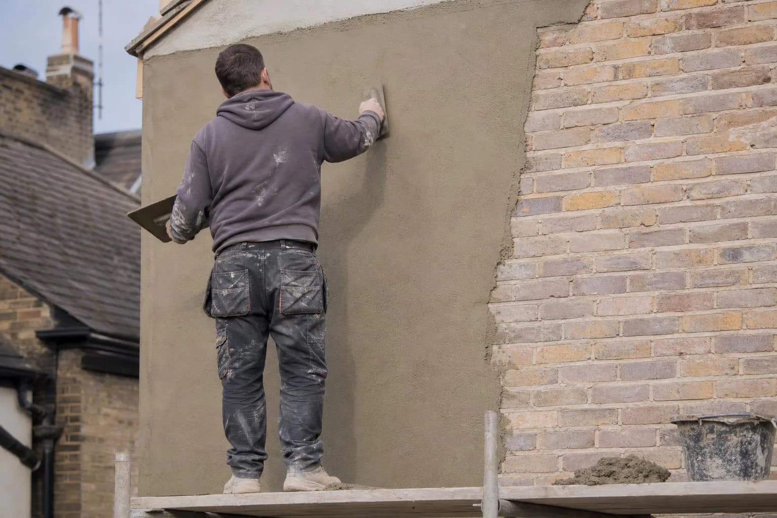 A plasterer applying render to an outside wall with a hawk and trowel