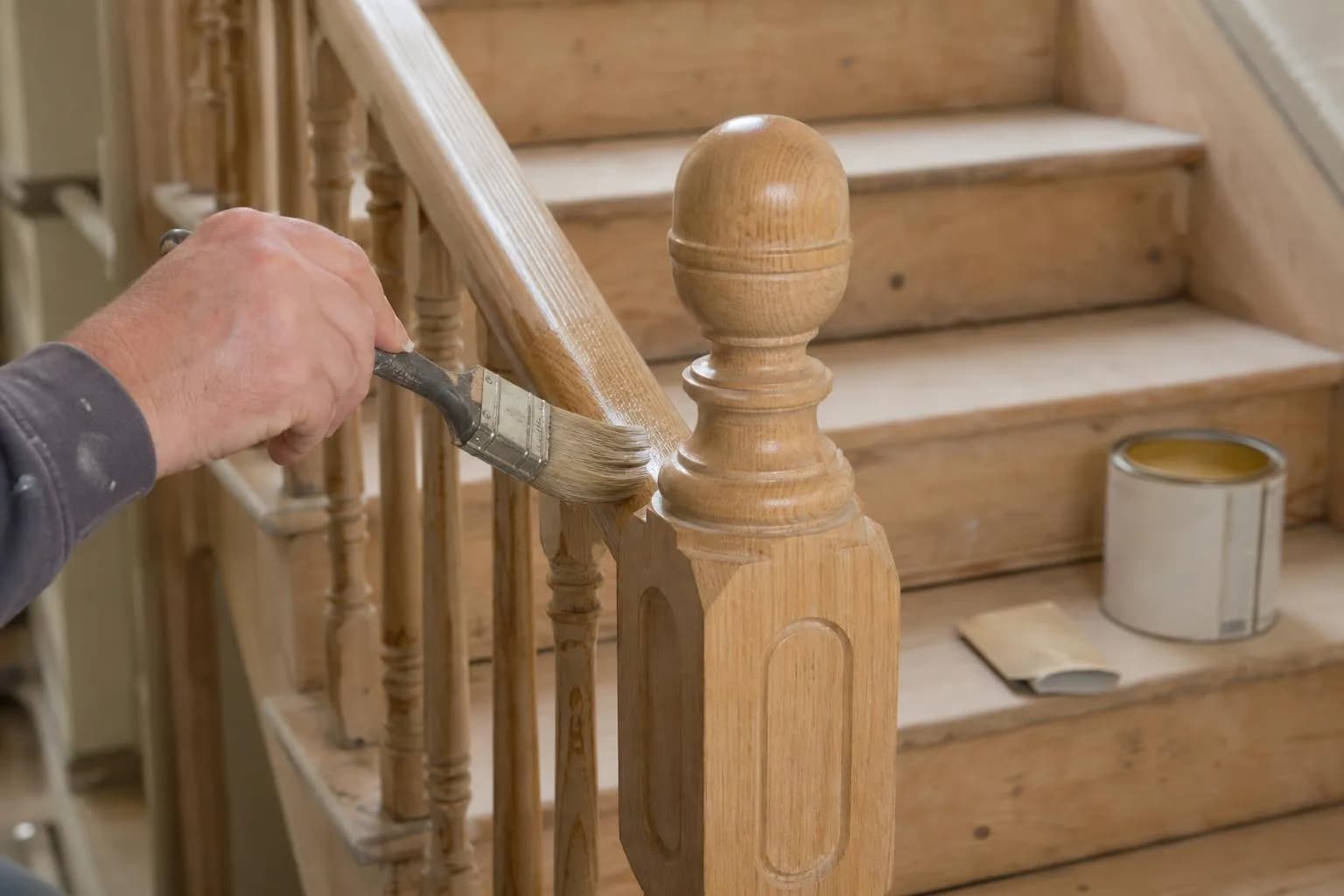 A decorator brushing varnish onto a stripped oak handrail and newel post