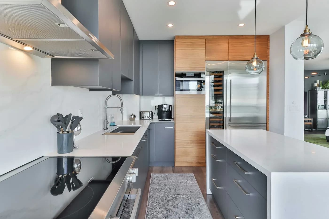 A renovated galley kitchen with grey units, white worktops and timber tall cabinets