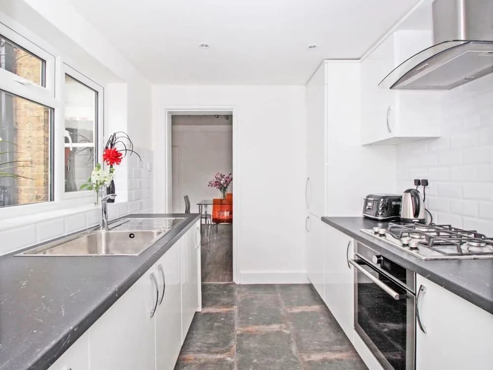 Galley kitchen with white gloss units, a dark grey worktop, white metro tiles and a slate floor