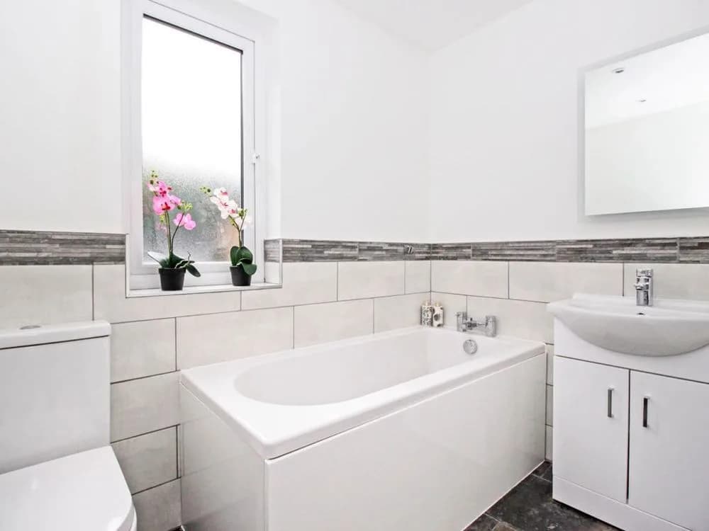 Bathroom with a bath, pale grey half-height tiles with a border and a white vanity unit