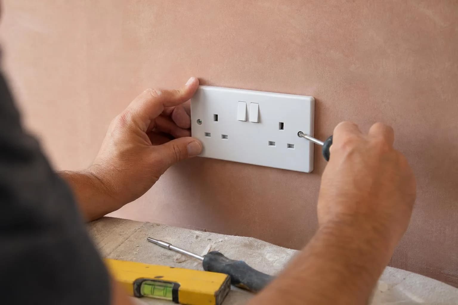 A new double socket being screwed into a freshly plastered wall, a spirit level beside it