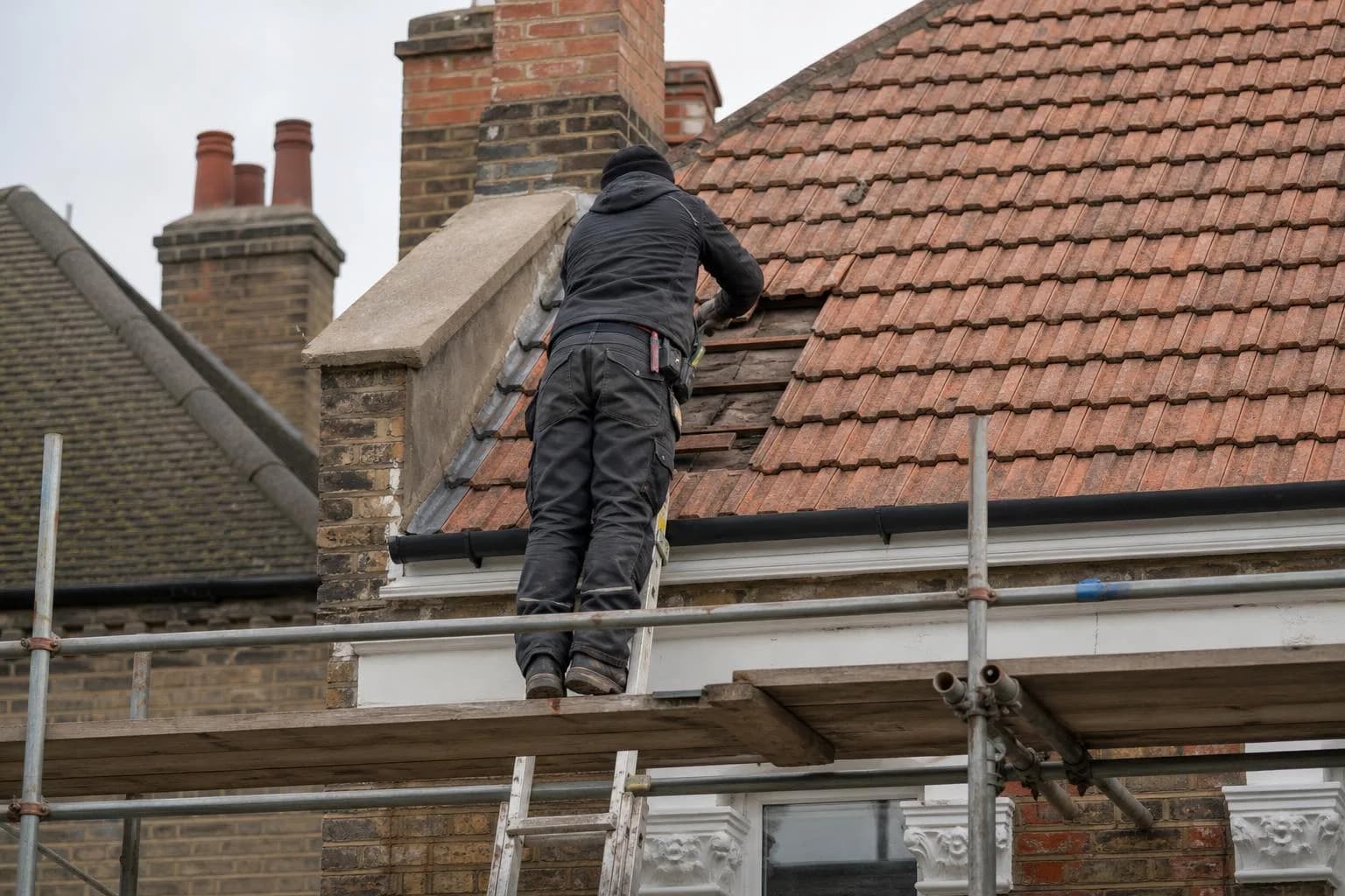 A roofer on a roof ladder replacing slipped tiles on a pitched roof